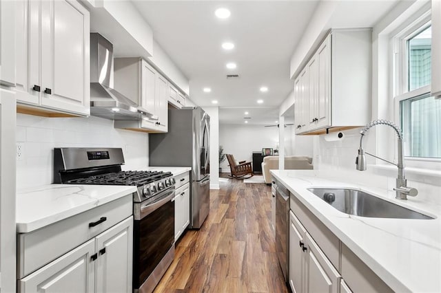 kitchen featuring appliances with stainless steel finishes, wall chimney exhaust hood, a sink, recessed lighting, and wood finished floors