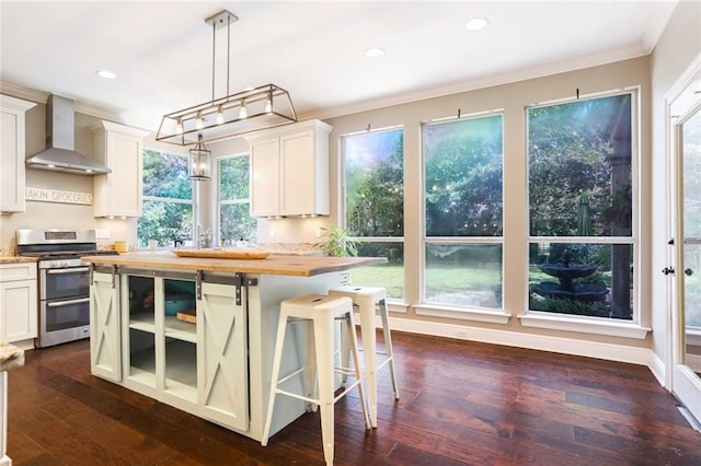 kitchen with double oven range, wall chimney range hood, ornamental molding, butcher block countertops, and recessed lighting