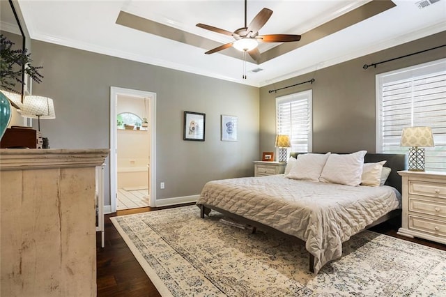 bedroom featuring a tray ceiling, dark wood-type flooring, crown molding, baseboards, and ensuite bathroom