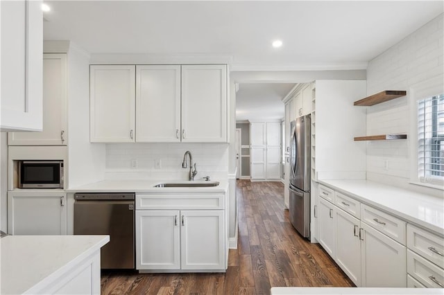 kitchen featuring appliances with stainless steel finishes, a sink, white cabinetry, dark wood finished floors, and backsplash