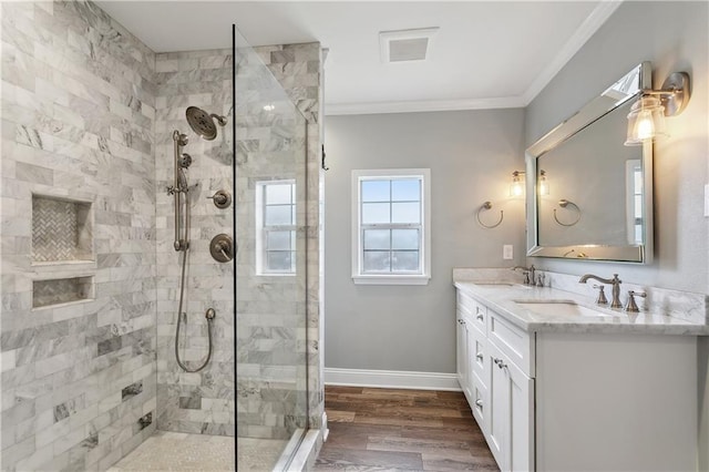 full bath featuring crown molding, tiled shower, baseboards, wood finished floors, and double vanity