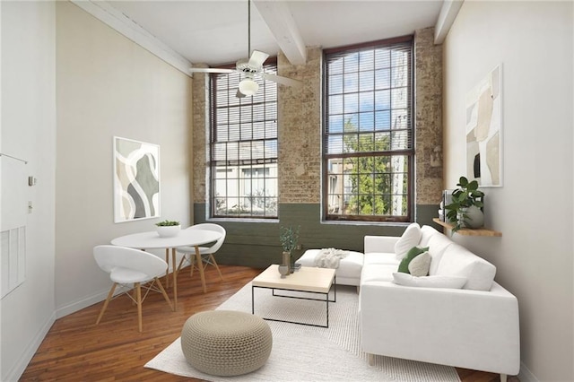 living area featuring wood finished floors, beam ceiling, baseboards, and a ceiling fan