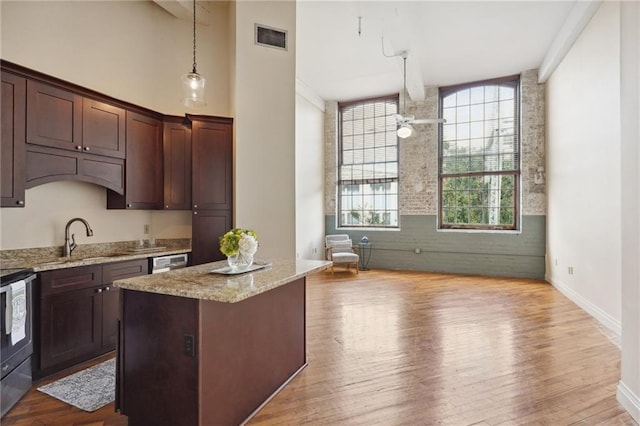 kitchen featuring a sink, decorative light fixtures, a kitchen island, wood finished floors, and a towering ceiling