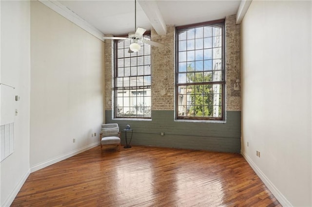 spare room with wood finished floors, beam ceiling, a ceiling fan, and baseboards