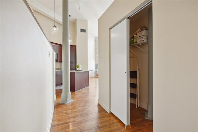 hallway with decorative columns, light wood-style flooring, and a towering ceiling