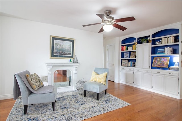 sitting room featuring light wood-style flooring, a fireplace, ceiling fan, built in shelves, and baseboards