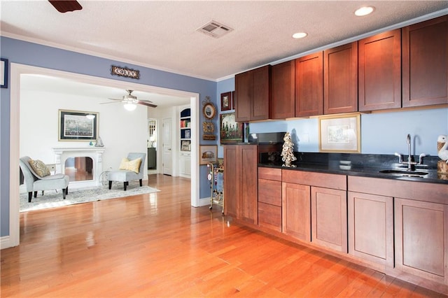 kitchen featuring a sink, dark countertops, light wood-type flooring, ceiling fan, and crown molding