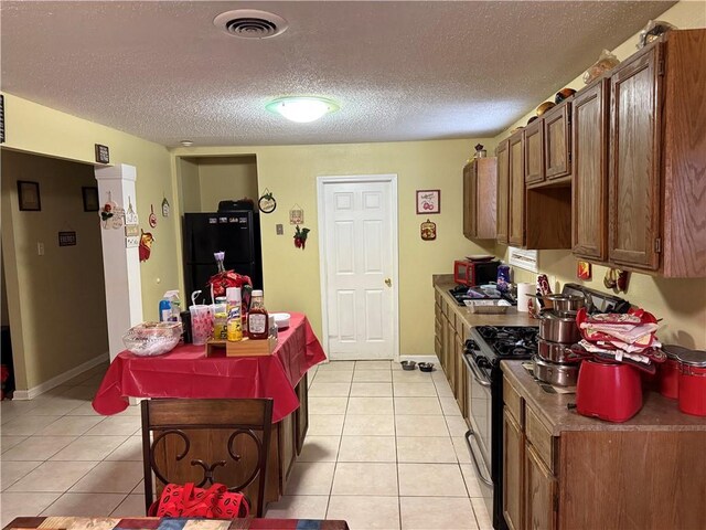 kitchen featuring freestanding refrigerator, light tile patterned floors, a textured ceiling, range with gas stovetop, and baseboards