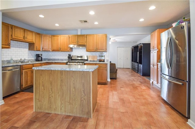 kitchen with appliances with stainless steel finishes, under cabinet range hood, light wood-style flooring, tasteful backsplash, and a sink