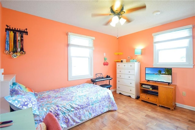 bedroom with multiple windows, light wood finished floors, baseboards, and ceiling fan
