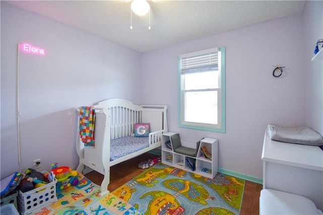 bedroom featuring wood finished floors, a crib, baseboards, and ceiling fan