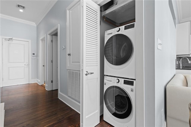 washroom featuring stacked washing machine and dryer, crown molding, dark wood-style flooring, and baseboards