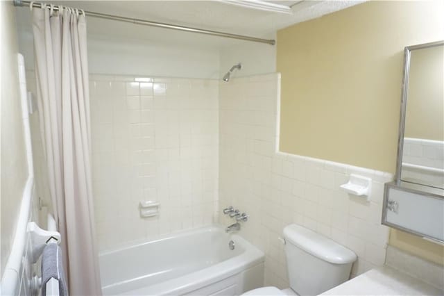 full bathroom featuring shower / tub combo, toilet, wainscoting, and tile walls