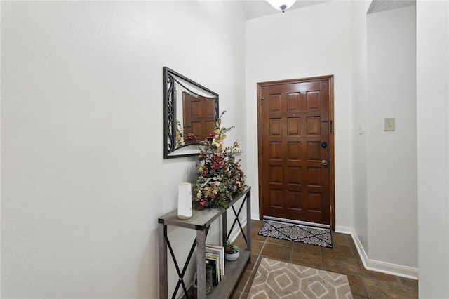 doorway to outside with baseboards and dark tile patterned floors