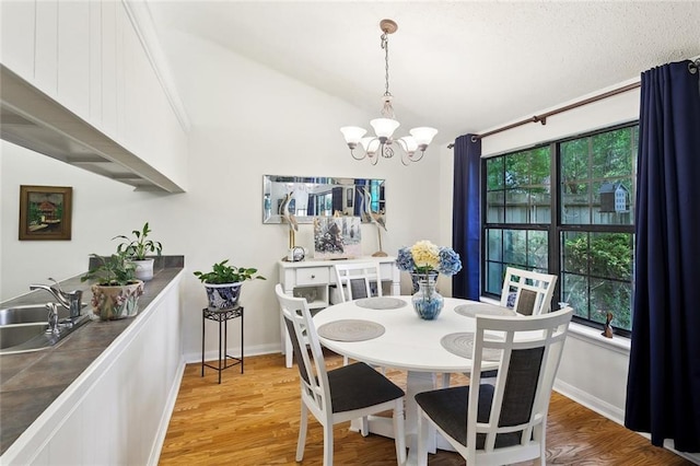 dining area featuring a chandelier, light wood-style flooring, vaulted ceiling, and baseboards