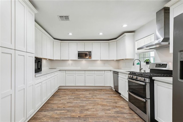 kitchen with appliances with stainless steel finishes, a sink, wall chimney exhaust hood, light countertops, and recessed lighting
