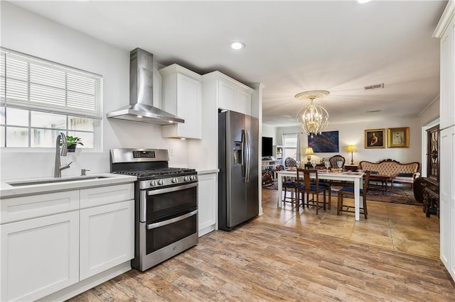 kitchen with stainless steel appliances, wall chimney exhaust hood, a sink, a chandelier, and light countertops