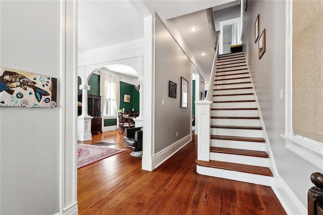 stairway with arched walkways, ornate columns, hardwood / wood-style floors, and baseboards