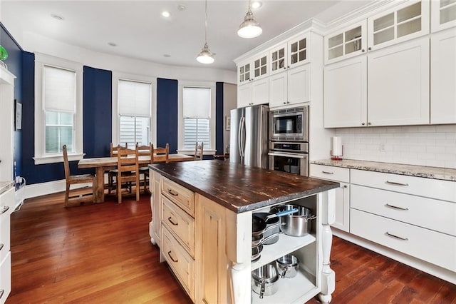 kitchen with appliances with stainless steel finishes, tasteful backsplash, dark wood-style floors, butcher block countertops, and pendant lighting