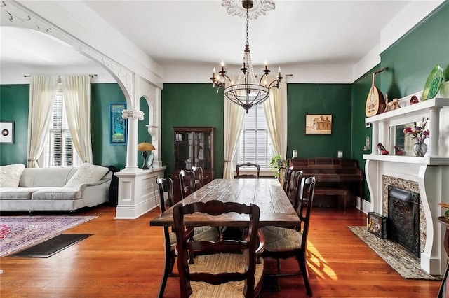 5925 Annunciation St, New Orleans, LA 70115 - dining space with a chandelier, arched walkways, wood finished floors, decorative columns, and a fireplace