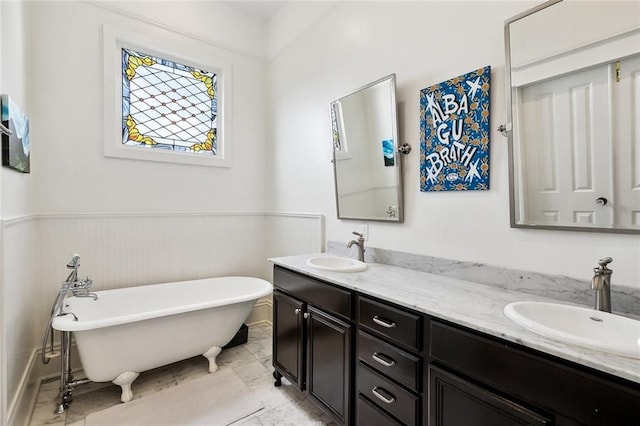 full bath featuring double vanity, a freestanding bath, wainscoting, and marble look tiles