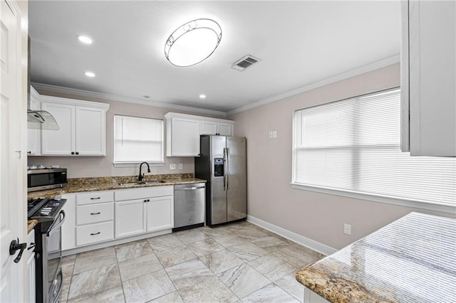 kitchen with appliances with stainless steel finishes, a sink, crown molding, dark stone countertops, and white cabinetry