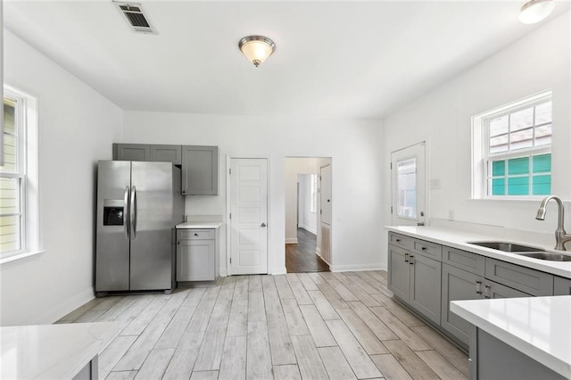 kitchen with stainless steel fridge with ice dispenser, gray cabinets, a sink, and light wood-style floors