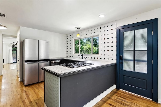 527 S Filmore St, Covington, LA 70433 - kitchen featuring stainless steel appliances, a peninsula, light wood-style floors, decorative light fixtures, and baseboards