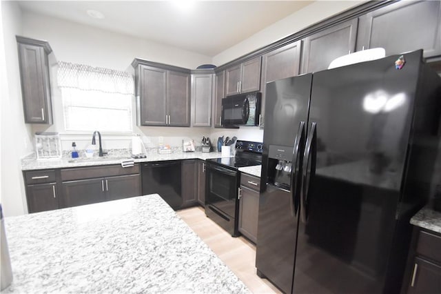kitchen featuring black appliances, a sink, light wood-style floors, dark brown cabinets, and light stone counters