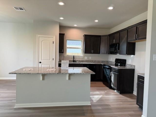 kitchen featuring black appliances, a kitchen island, light stone counters, light wood finished floors, and recessed lighting
