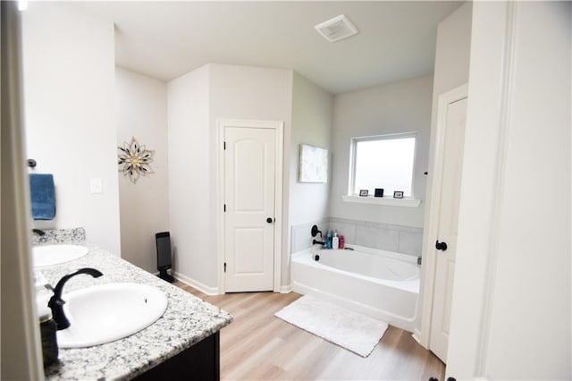 full bath with wood finished floors, a bath, double vanity, and baseboards