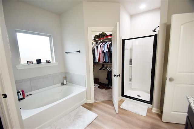 full bathroom with a shower stall, wood finished floors, a bath, a walk in closet, and vanity