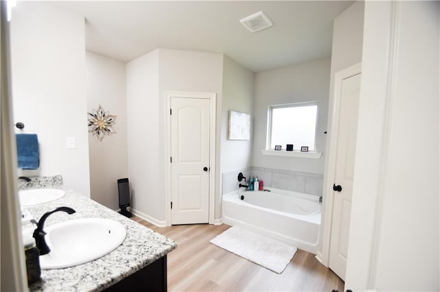 full bath featuring wood finished floors, double vanity, a garden tub, and baseboards