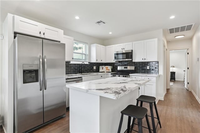 240810 Saint Anthony St, New Orleans, LA 70119 - kitchen with stainless steel appliances, a sink, white cabinetry, backsplash, and a kitchen breakfast bar