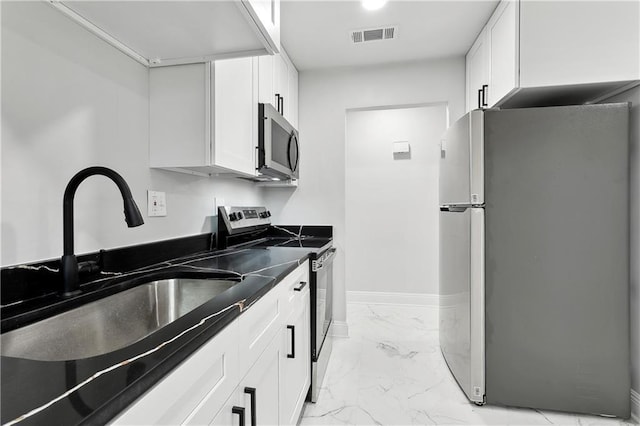 kitchen with appliances with stainless steel finishes, light marble finish flooring, white cabinets, a sink, and dark countertops