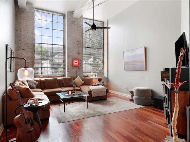 living room featuring wood finished floors, a high ceiling, healthy amount of natural light, baseboards, and ceiling fan