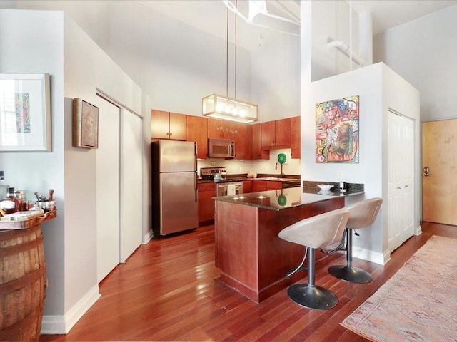 kitchen featuring stainless steel appliances, dark countertops, a peninsula, wood finished floors, and a towering ceiling