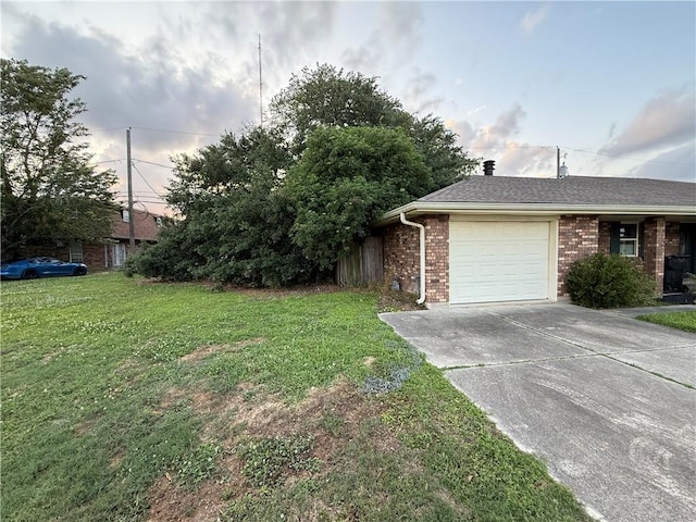 view of side of home featuring brick siding, an attached garage, a yard, and driveway