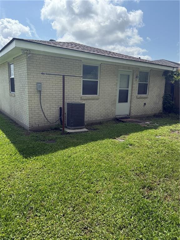 rear view of property with brick siding, central AC unit, and a lawn