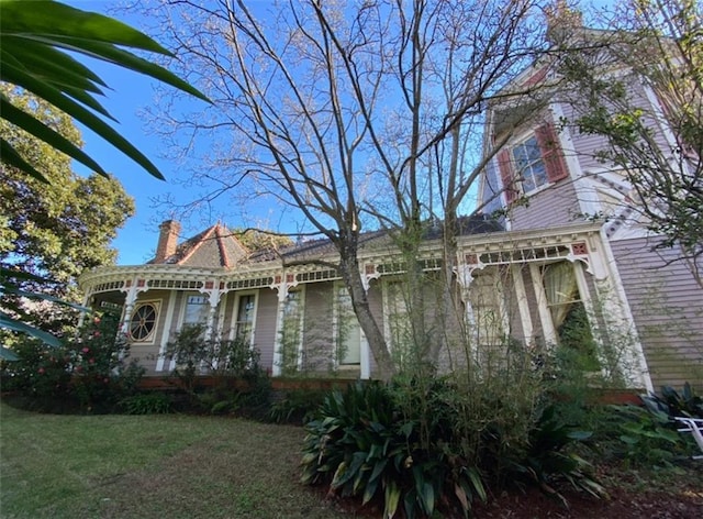 view of property exterior featuring a chimney, a lawn, and covered porch