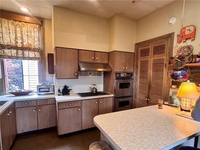 kitchen with double wall oven, under cabinet range hood, gas cooktop, a peninsula, and backsplash