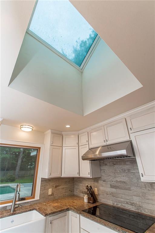 156 Oak Holw, Hammond, LA 70401 - kitchen featuring under cabinet range hood, a sink, black electric cooktop, white cabinetry, and a skylight