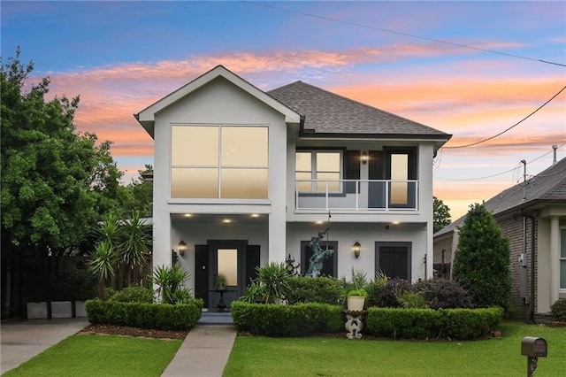 contemporary home featuring a balcony, stucco siding, and a lawn
