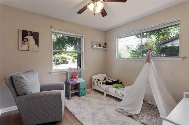 bedroom featuring multiple windows, baseboards, wood finished floors, and ceiling fan