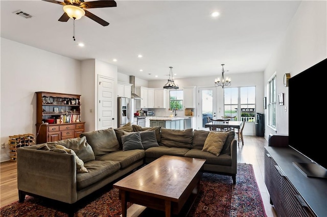 living area with light wood-style floors, a ceiling fan, a chandelier, and recessed lighting