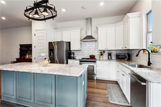 kitchen with wall chimney range hood, appliances with stainless steel finishes, a sink, a kitchen island, and decorative backsplash