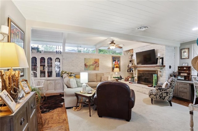 carpeted living room with brick wall, ceiling fan, a fireplace, and beam ceiling