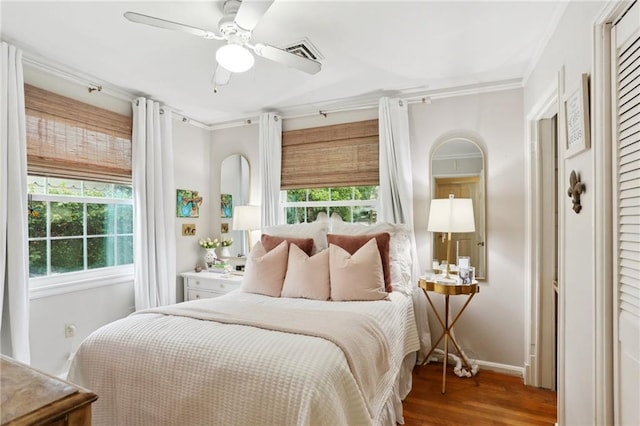 bedroom featuring multiple windows, wood finished floors, crown molding, baseboards, and a ceiling fan