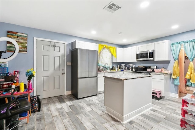 3017 Music St, New Orleans, LA 70122 - kitchen featuring appliances with stainless steel finishes, light wood-type flooring, recessed lighting, white cabinetry, and a center island