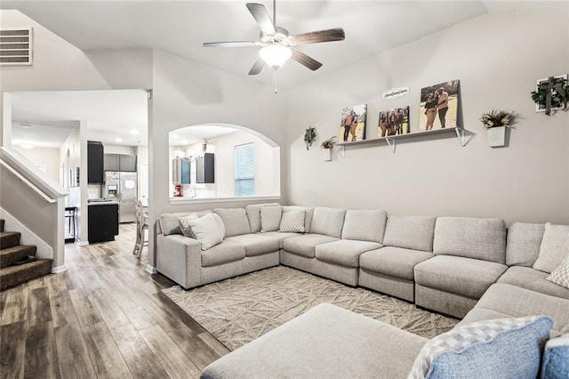 living area with ceiling fan, light wood finished floors, lofted ceiling, stairs, and arched walkways